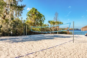 A beach volleyball court with a net, surrounded by sand and trees. - Second floor condo w/ gym, shared pools, tennis court - near theme parks (Davenport)