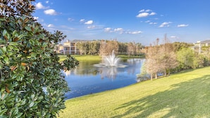Ein friedlicher Park mit Teich, Springbrunnen und Gebäuden im Hintergrund.
