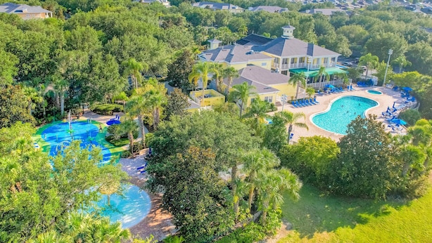 An aerial view of a residential area with multiple houses, a large swimming pool, and lush greenery. - 2nd floor condo w/ gym, shared pools, tennis court, balcony, sauna (Davenport)