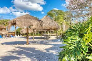 A beach with thatched umbrellas, lounge chairs, and a sandy area. - 1st floor condo near theme parks, pools, tennis court, gym (Davenport)