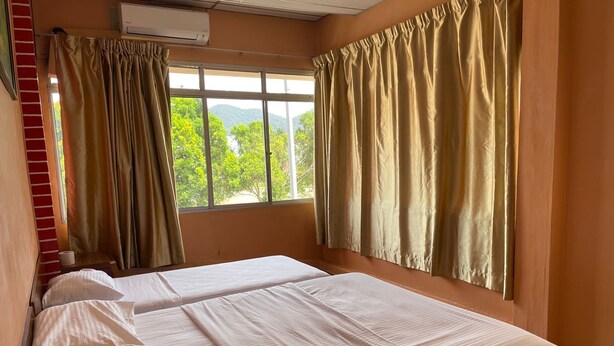 Une chambre avec deux lits, des rideaux beiges et une fenêtre donnant sur un paysage verdoyant.