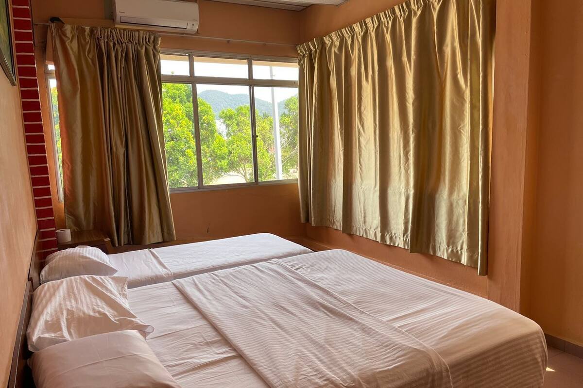 A bedroom with two beds, beige curtains, and a window with a view of greenery.