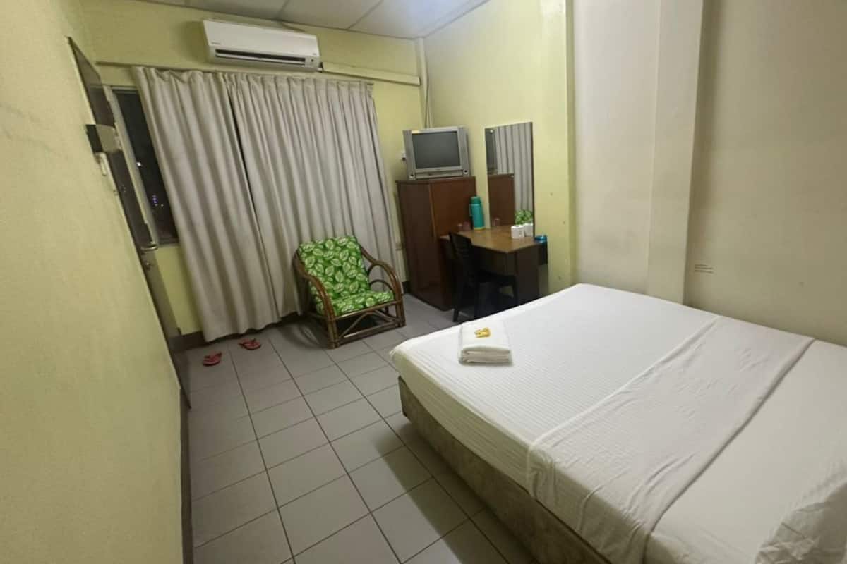 A hotel room with a bed, a chair, a desk with a computer, and an air conditioning unit.
