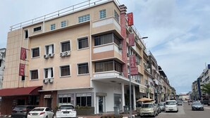 Un hôtel à plusieurs étages avec un restaurant au rez-de-chaussée, plusieurs voitures garées et un ciel dégagé.