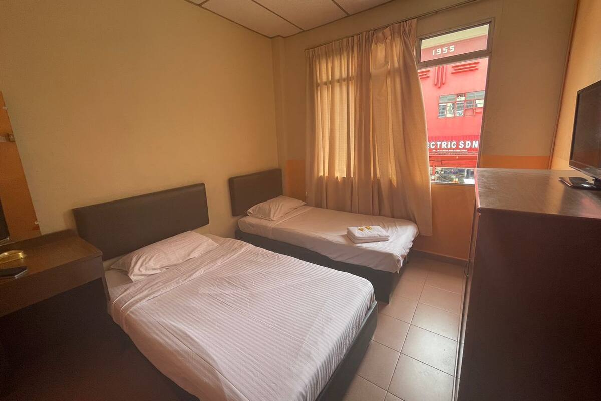 A hotel room with two beds, a desk, and a window with curtains.