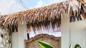 Une porte en bois ornée d’une serrure en métal décorative, entourée d’une végétation luxuriante et surmontée d’un toit de chaume.
