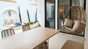 Un espace repas extérieur moderne, avec une table et des chaises en bois, un fauteuil suspendu en osier, et une piscine visible à travers les portes vitrées.