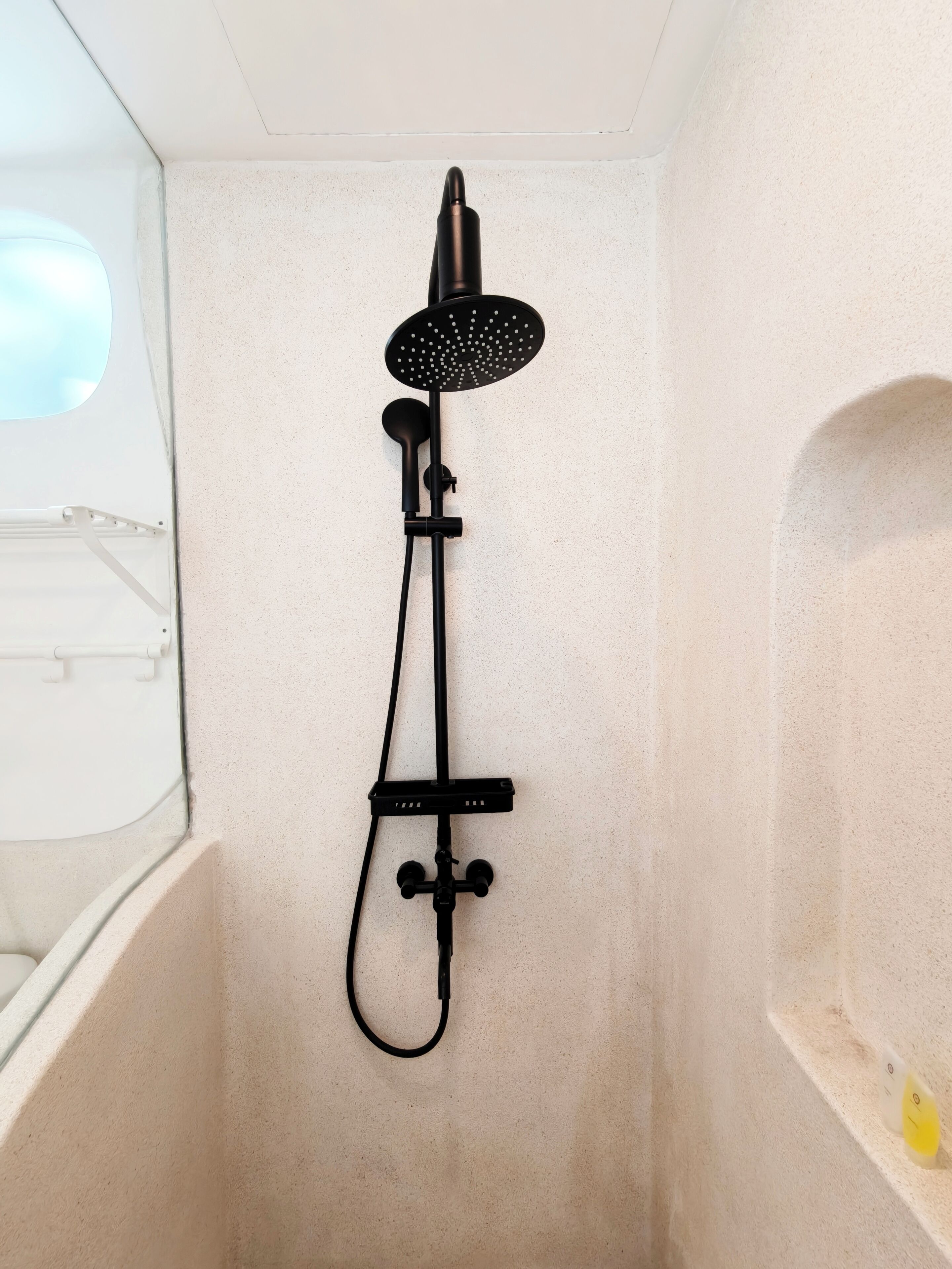 A shower with a handheld showerhead and a handheld scrubber mounted on the wall.
