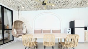 Un espace repas moderne avec un plafond haut, un fauteuil suspendu, une longue table à manger et des chaises en osier.