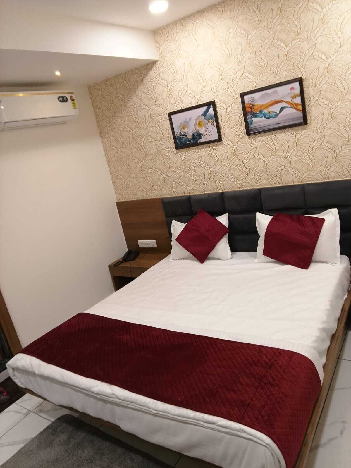 Habitación de hotel con cama, mesita de noche, equipo de aire acondicionado y dos cuadros en la pared.