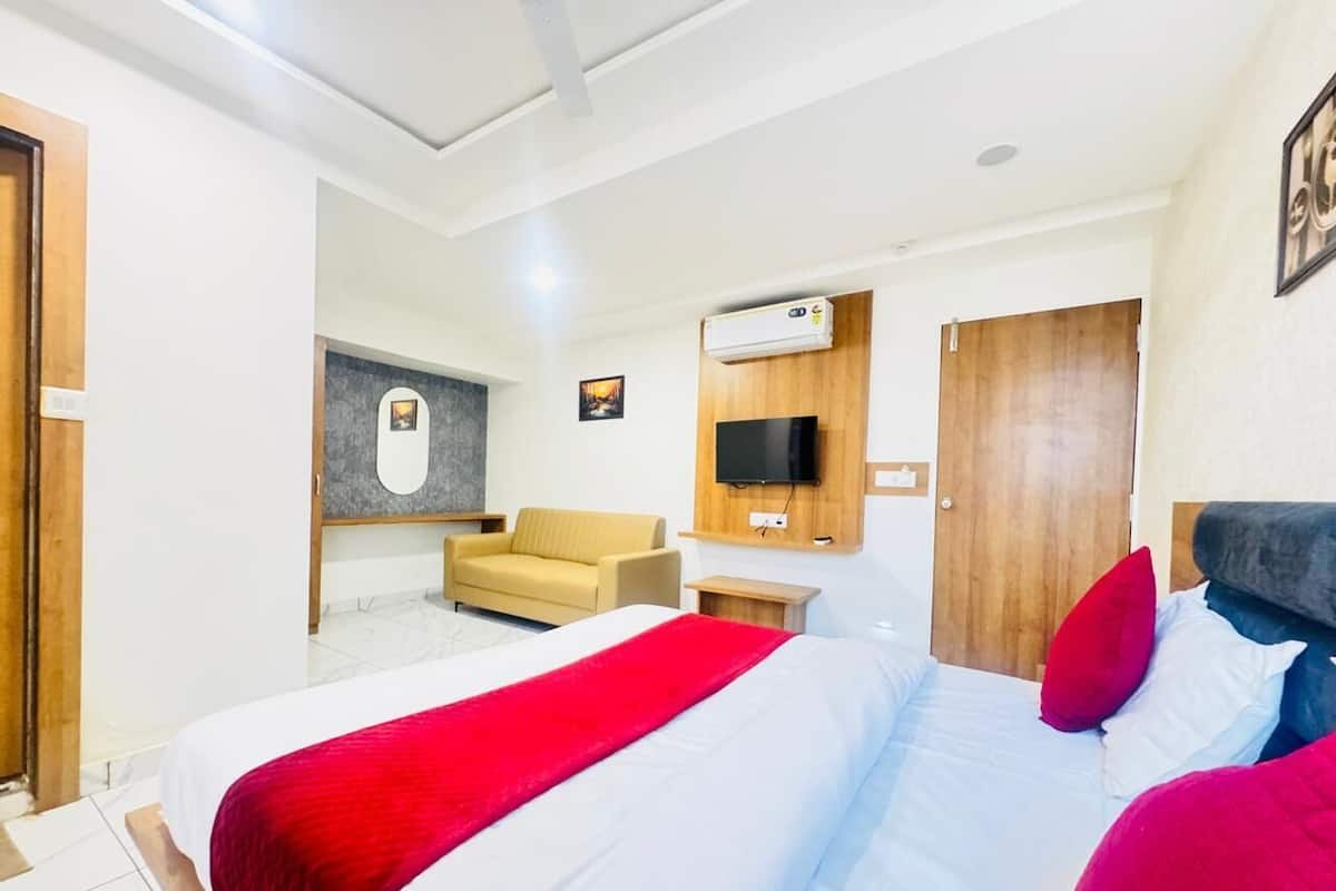 A modern hotel room with a large bed, a sofa, a TV mounted on the wall, and a wooden door.