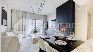 A modern living room with a sofa, dining table set with plates and glasses, and a fireplace. - Bloomfields Formula 1br In Water (Abu Dhabi)