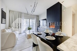 A modern living room with a sofa, dining table set with plates and glasses, and a fireplace. - Bloomfields Formula 1br In Water (Abu Dhabi)
