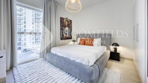 A modern bedroom with a large bed, a view of the city through a window, and a pendant light. - Bloomfields Formula 1br In Water (Abu Dhabi)