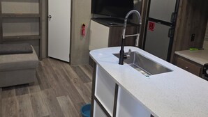 Uma cozinha compacta com pia embutida, televisão de tela plana, relógio e extintor de incêndio.