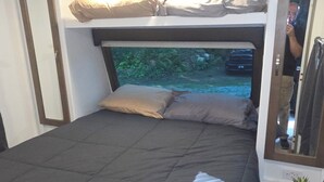 Quarto compacto com uma cama de solteiro, uma cama individual, uma pequena planta em vaso e um espelho.