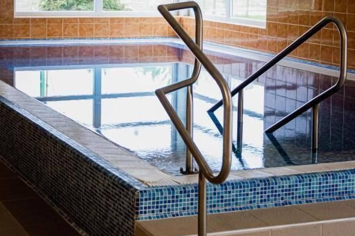 Ein Innenpool mit großen Glaswänden, Metallhandläufen und Blick auf Grünflächen.