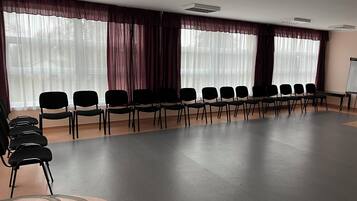 Un salón de conferencias con filas de sillas, ventanas amplias con cortinas translúcidas y una pizarra.