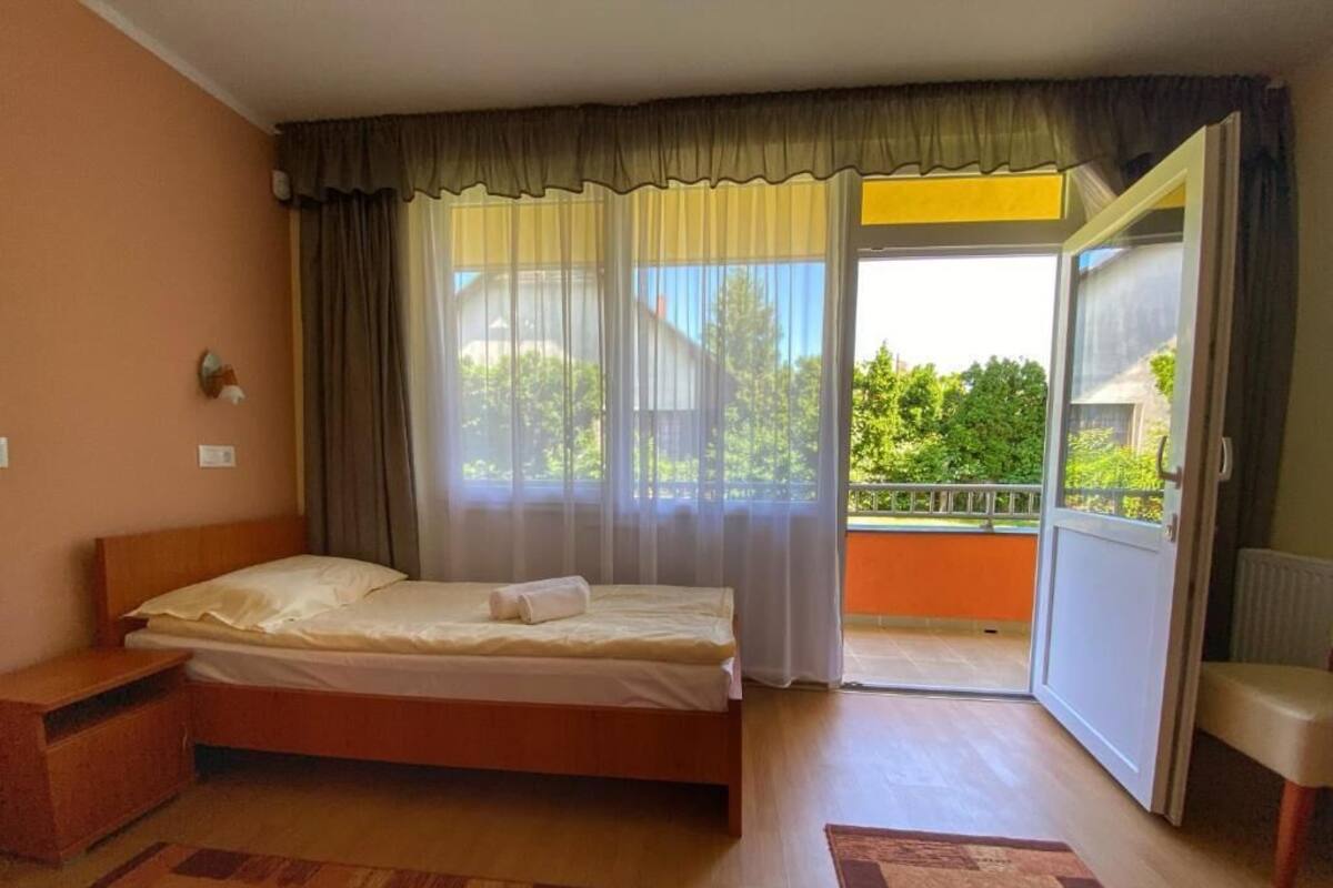 Ein Schlafzimmer mit einem Bett, einem Nachttisch, einem Fenster mit Vorhängen und Blick auf einen Balkon.