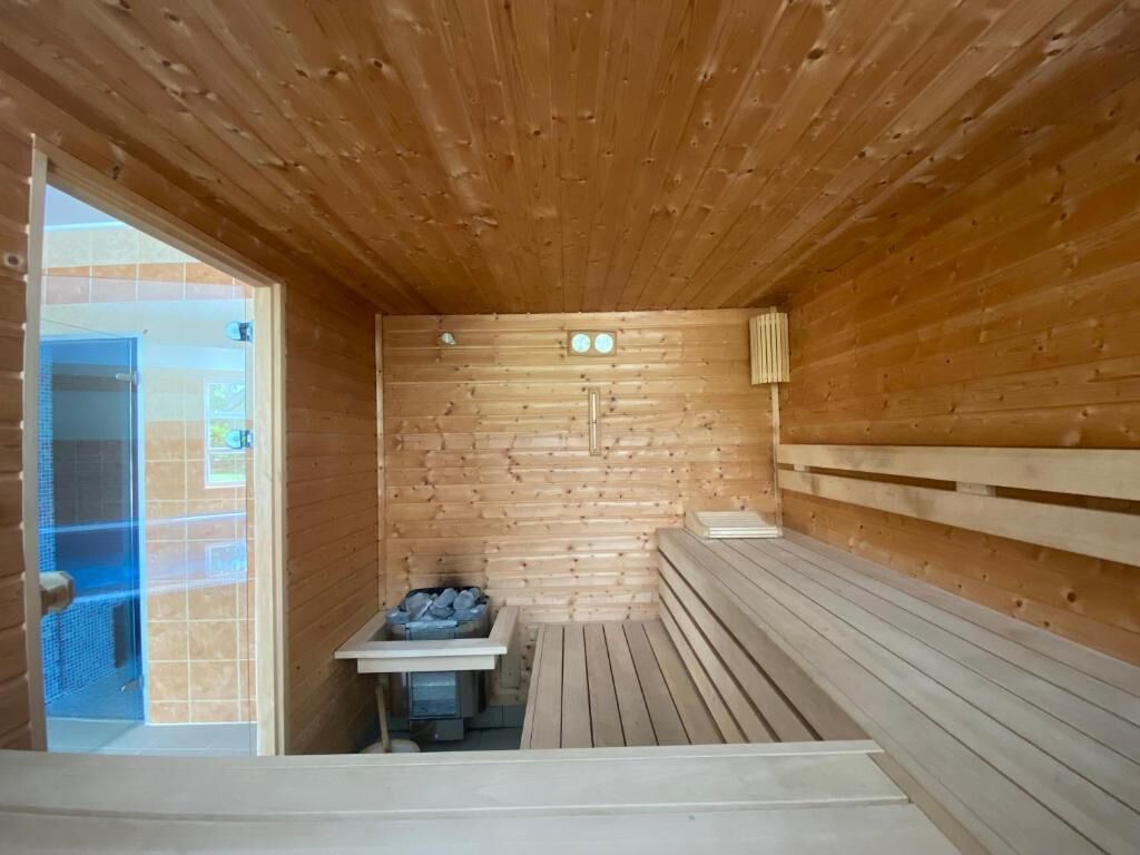 Ein Saunaraum mit Holzwänden und Bänken, ein kleiner Tisch mit einem Heizgerät und eine Tür, die nach draußen führt.