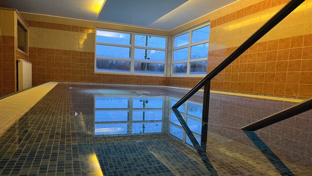 Une piscine intérieure aux murs carrelés, offrant une vue dégagée sur l’extérieur grâce à de grandes fenêtres.