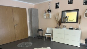 Une chambre moderne avec une armoire en bois, une commode blanche, une chaise et un miroir au mur.