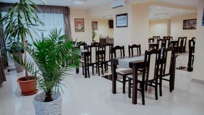 Un espace de restauration d’hôtel comprenant plusieurs tables et chaises, des plantes en pot et des œuvres d’art encadrées accrochées aux murs.