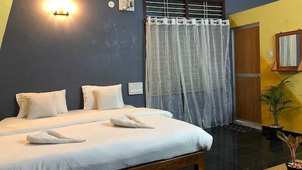 A hotel room with a bed, a bedside table, a potted plant, and a window with curtains. - Nature Inn Cottage (Gokarna)