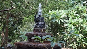 A tiered stone fountain with water spouting from the top, surrounded by lush greenery. - Nature Inn Cottage (Gokarna)