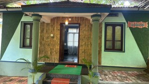 A building entrance with a wooden facade, a green and blue exterior, and a covered walkway leading to the door. - Nature Inn Cottage (Gokarna)