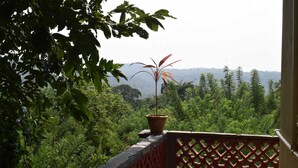A balcony with a potted plant, surrounded by dense greenery and a distant view of a hilly landscape. - Nature Inn Cottage (Gokarna)