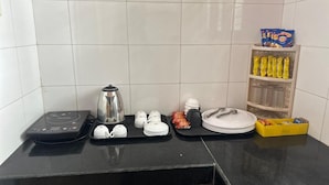 A kitchen counter with a coffee maker, tea set, plates, bowls, and a yellow basket with snacks. - Nature Inn Cottage (Gokarna)