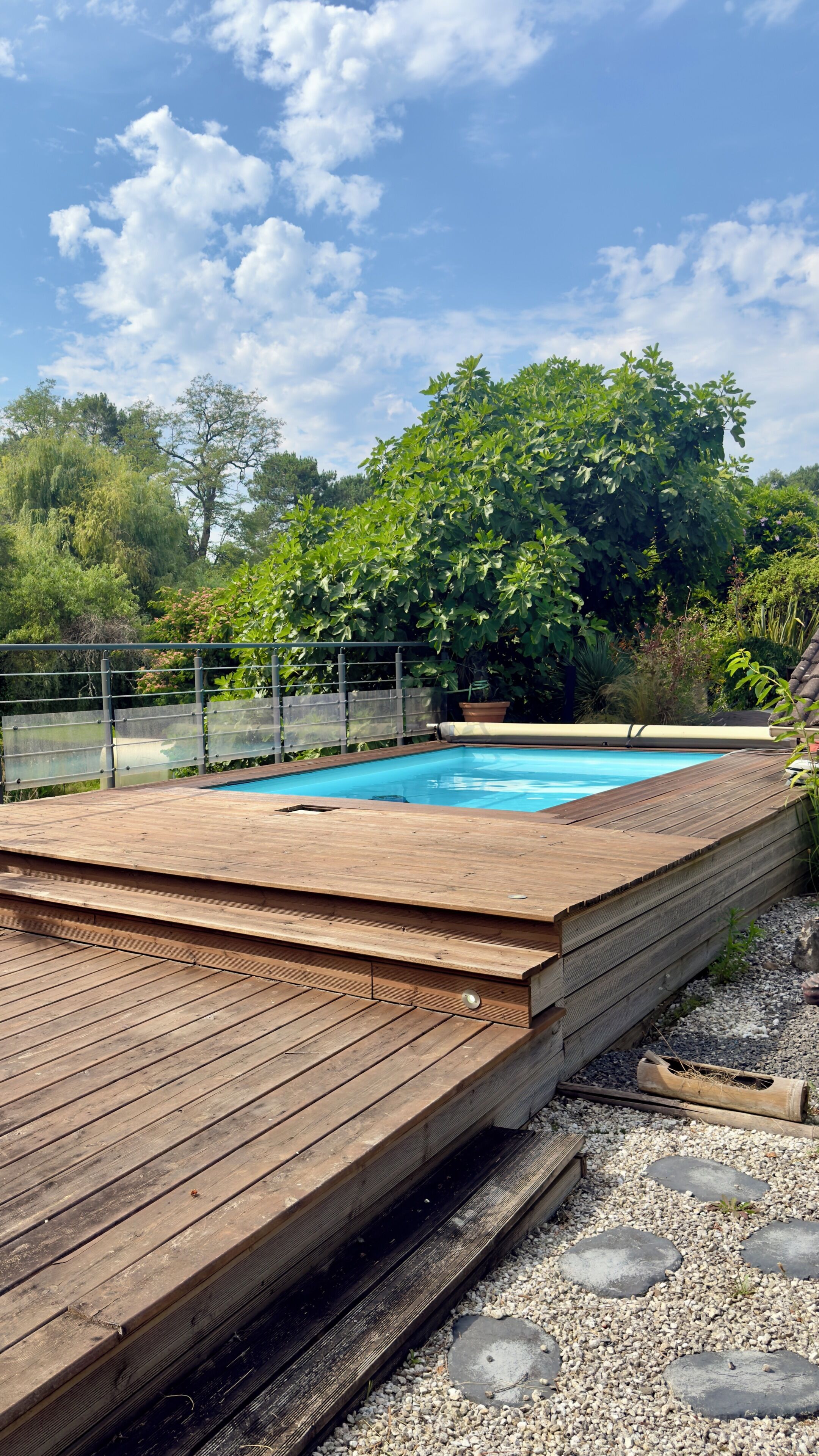 Eine Holzterrasse mit Swimmingpool, umgeben von Bäumen und einem Zaun.