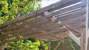 Une pergola en bois, avec une table et des chaises en dessous, entourée de verdure.