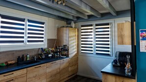 Une cuisine avec des meubles en bois, un plan de travail noir et une fenêtre avec des stores.