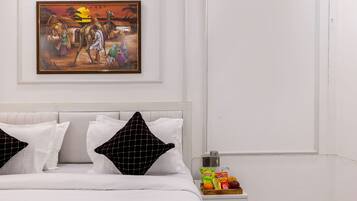 Una habitación de hotel con una cama, almohadas, una mesita de noche con aperitivos y un cuadro en la pared.