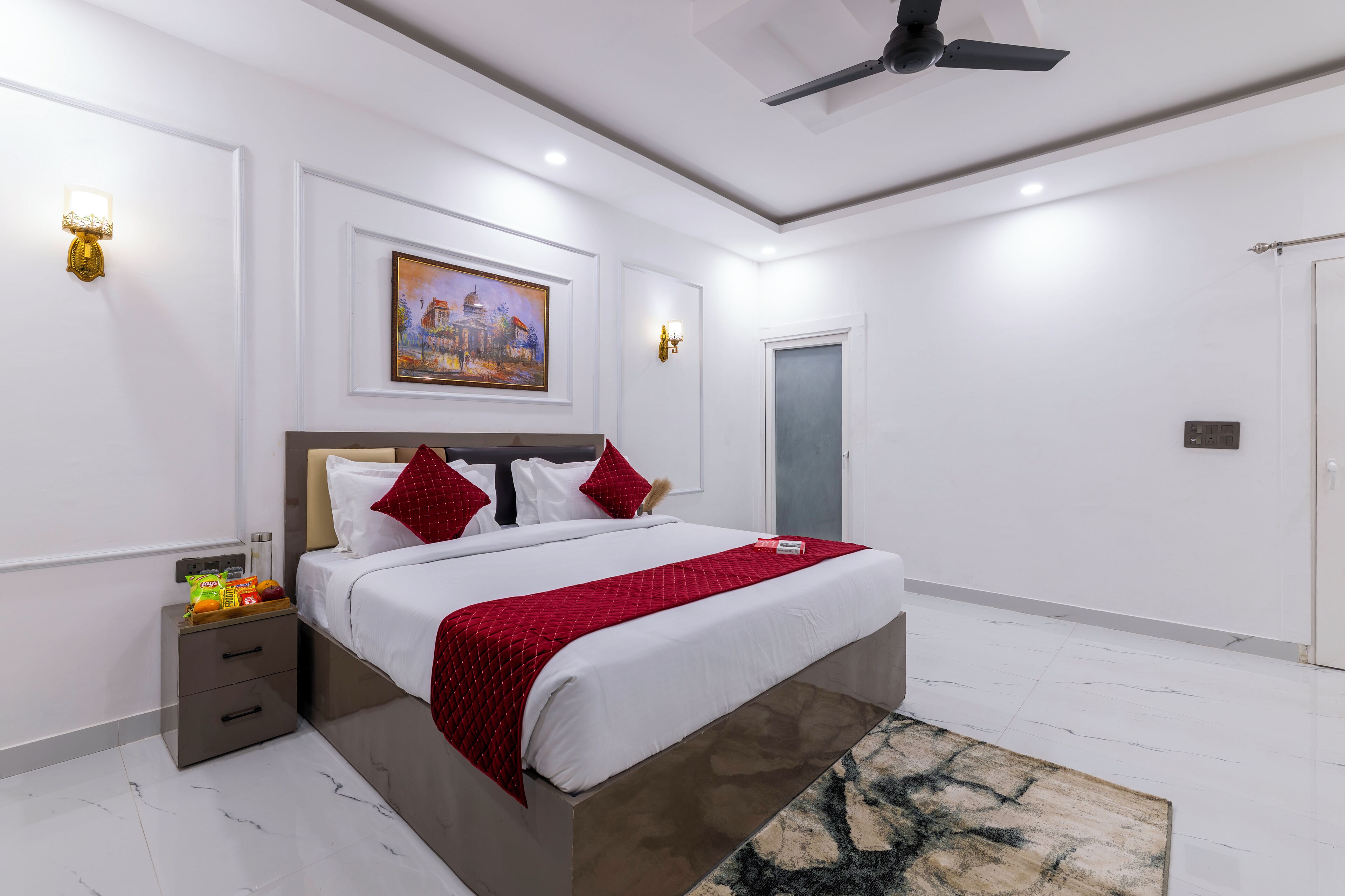 A modern bedroom with a large bed, a nightstand, a ceiling fan, and a painting on the wall.