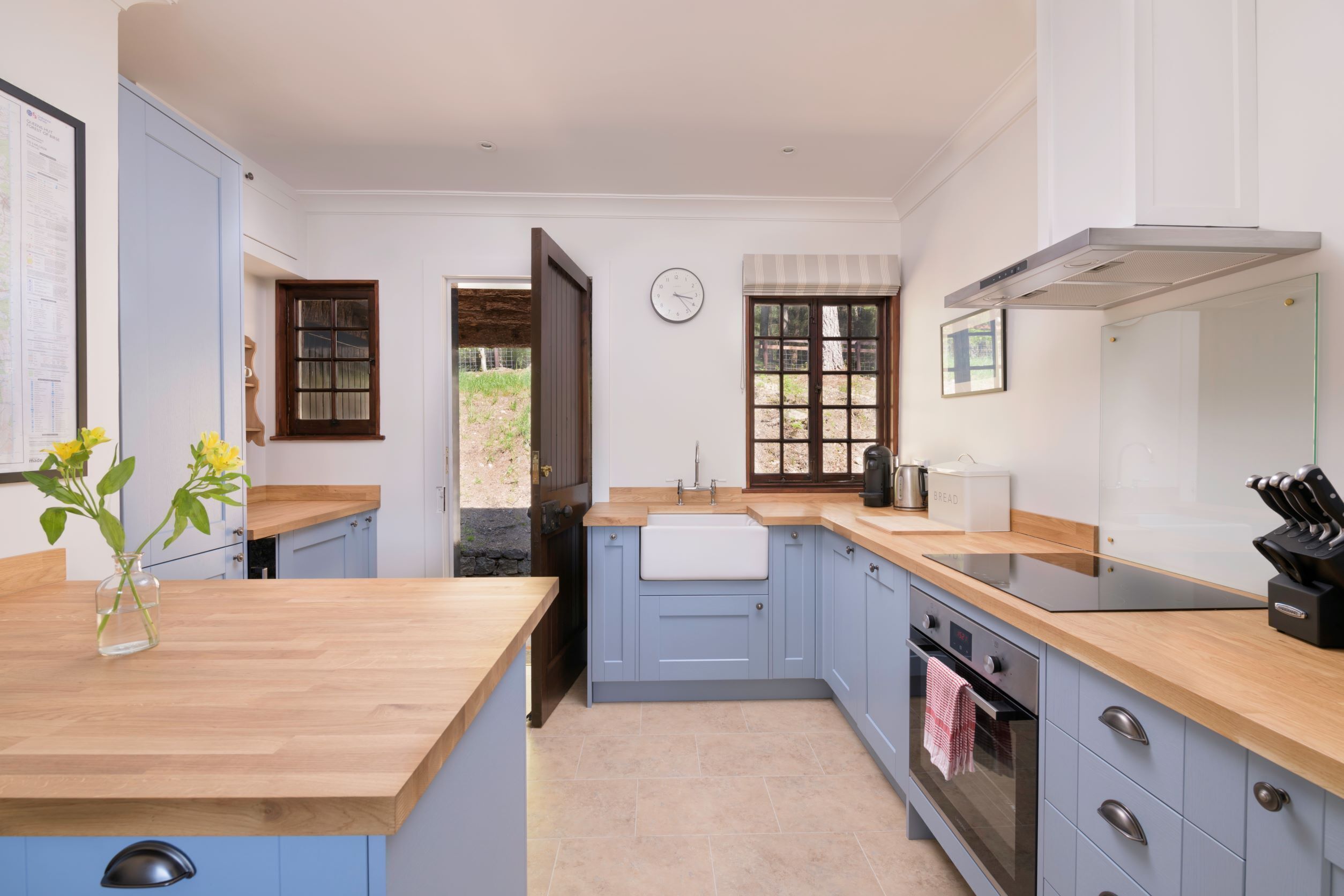A modern kitchen with blue cabinets, a wooden countertop, a built-in oven, and a window with a view of the outdoors.