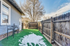 Un jardin avec une clôture en bois, une pelouse et une terrasse avec des chaises.