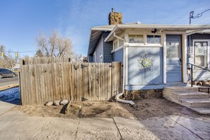 Une maison avec une clôture en bois, une cheminée en pierre et un petit porche avec des marches.