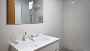 Ein modernes Badezimmer mit Waschbecken, Spiegel und Dusche, alles in Weiß.