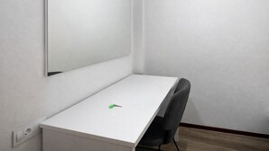 Ein kleiner, weißer Schreibtisch in L-Form mit einem Stuhl, einem grünen Schlüsselanhänger und einem an der Wand befestigten Spiegel.