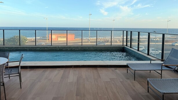 Zona de piscina con vista al océano y un edificio al fondo.