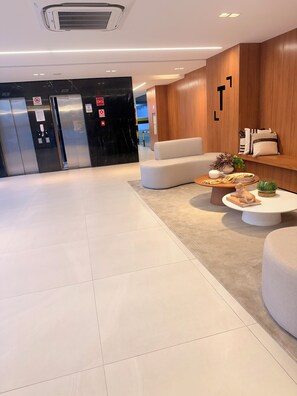 A modern lobby with a marble reception desk, a sofa, a coffee table with decorative items, and an elevator. - Ceci Home - Excellent location and sea view. (Salvador)