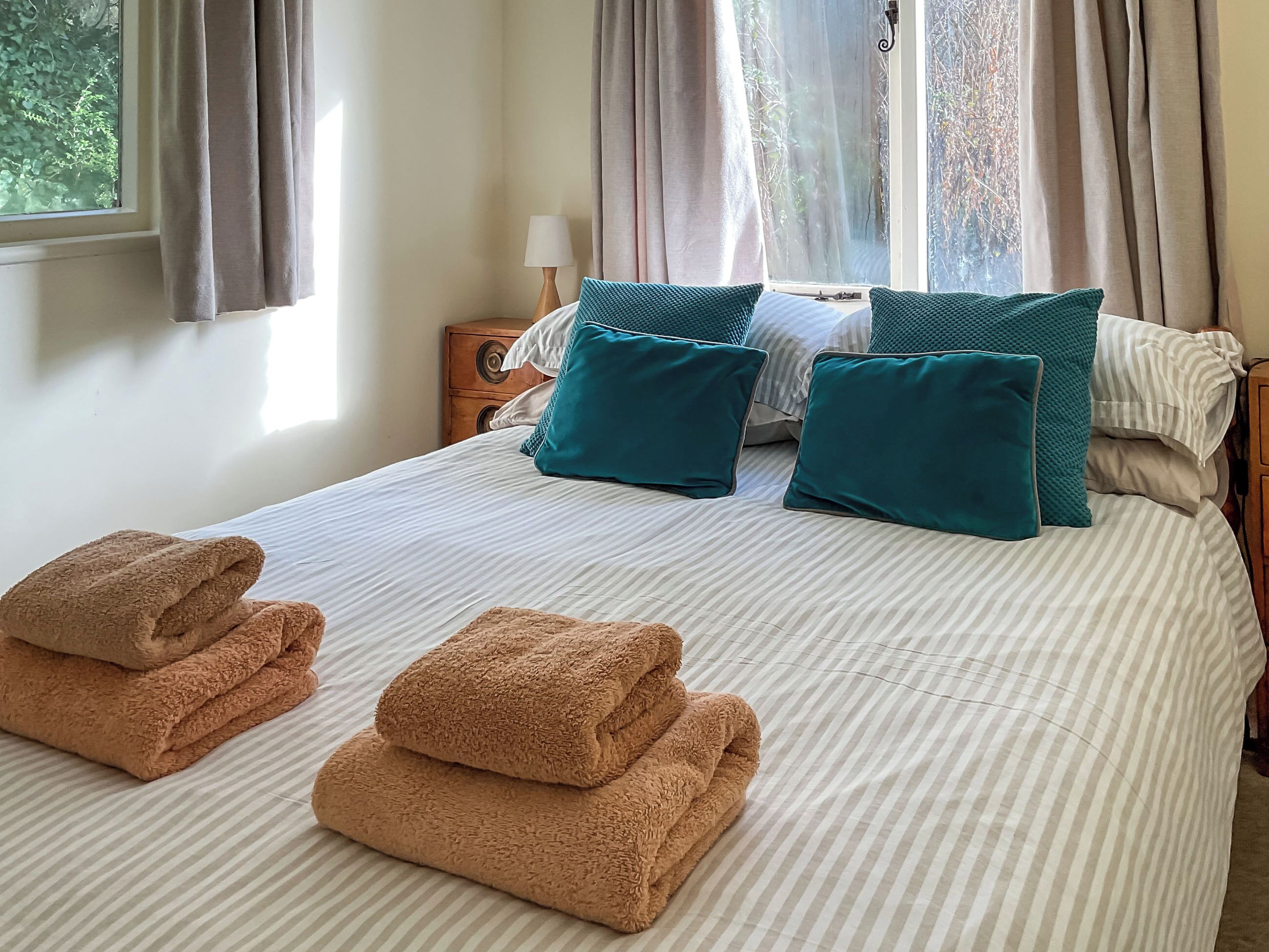 A neatly made bed with striped bedding, teal pillows, and folded towels.