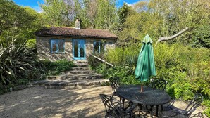 Un edificio de piedra con techo de tejas, una sombrilla verde y una mesa con sillas en un jardín.