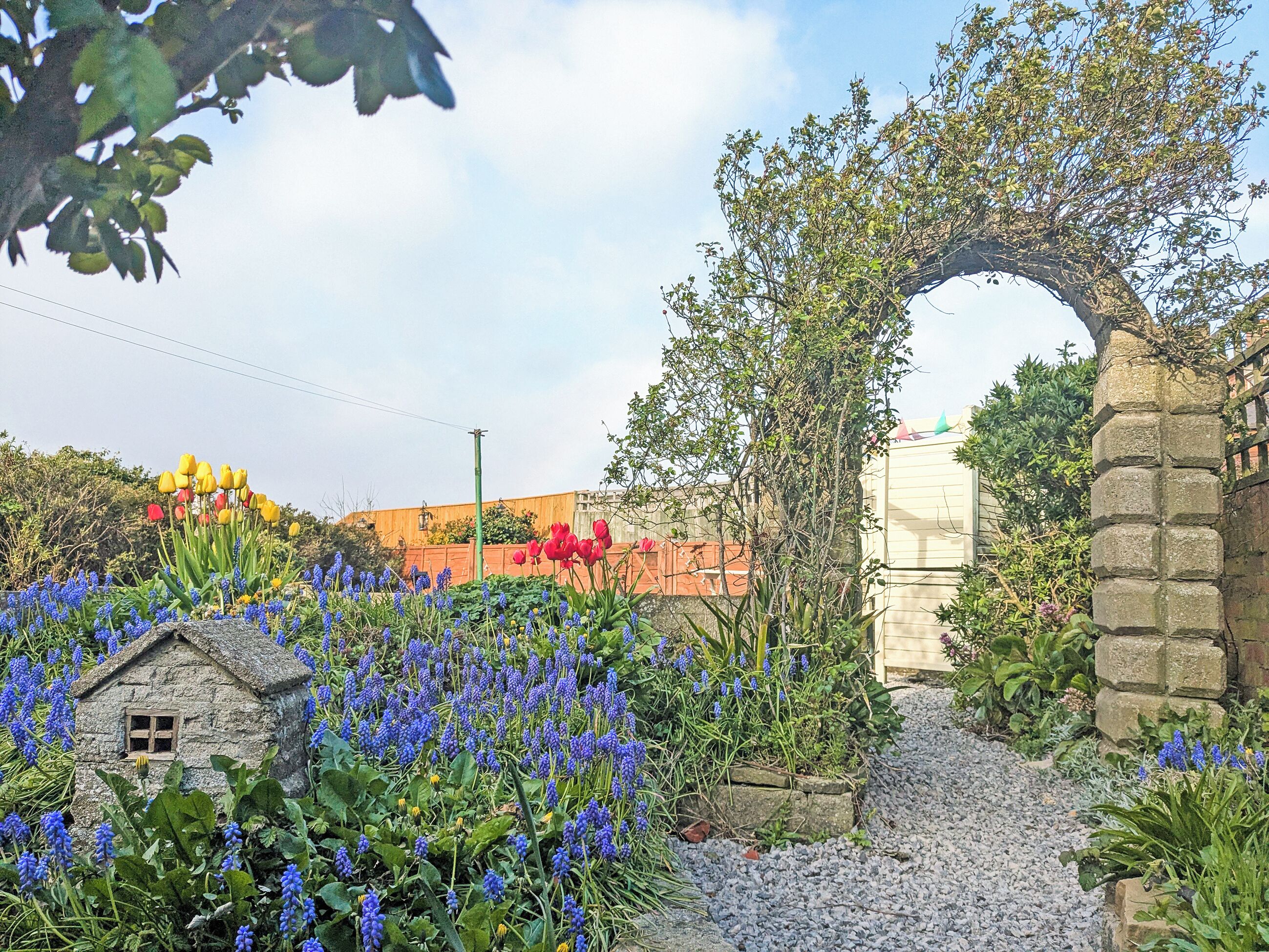 A garden with a stone archway, a small house, and various flowers.