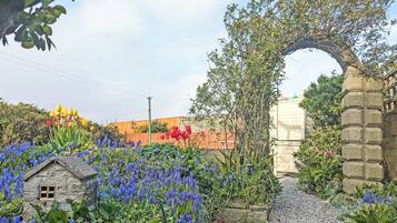 A garden with a stone archway, a small house, and various flowers.