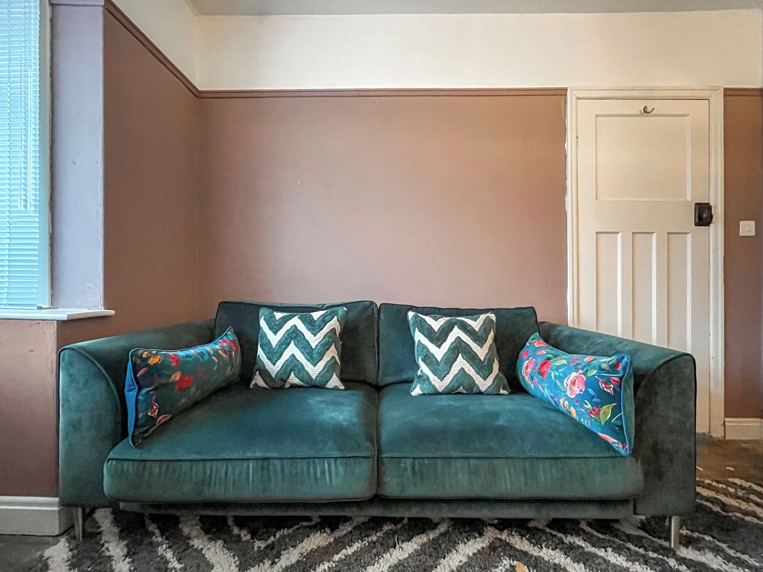 A teal sofa with patterned cushions in a room with a brown wall and a white door.