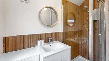 A bathroom with a white sink, wooden paneling, a round mirror, and a glass-enclosed shower.